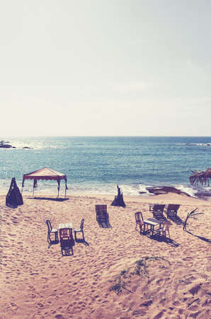 Empty tropical beach with tables and chairs, retro color toning applied.の写真素材