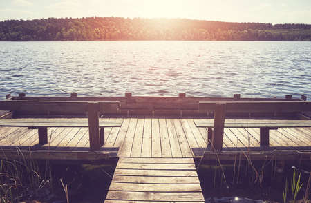 Wooden pier with benches at a lake against the sun, color toning applied.の写真素材