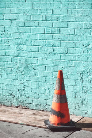 Old dirty traffic cone by a brick wall, selective focus, color toning applied.