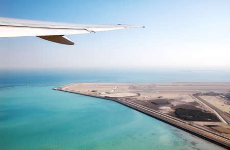 Wing of a plane above the sea and an airport, transport industry concept.の写真素材