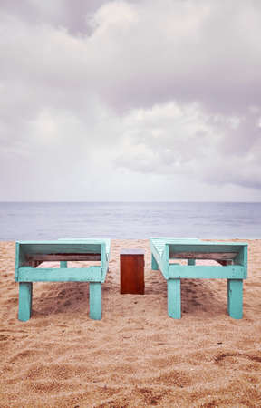 Wooden sunbeds on an empty beach on a rainy day, color toning applied.の写真素材
