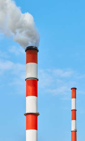 Red and white painted smoking chimneys against the blue sky.