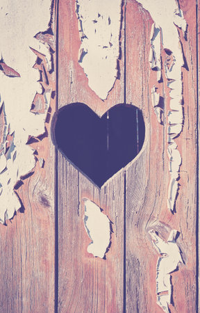 A heart shape cut out of a wooden board with peeling paint.の写真素材