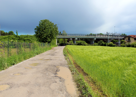 Rural unpaved road and green wheat field under a stormy skyの写真素材