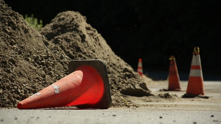 Four traffic cones by two large piles of dirt on the side of the road  The first cone is knocked overの写真素材