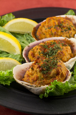 Stuffed seasoned clams garnished with romaine lettuce and lemon wedges on a rustic platterの写真素材