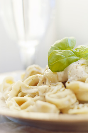 Cheese tortellini in a creamy alfredo sauce garnished with fresh basil leavesの写真素材