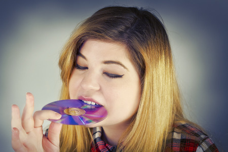 Young and cute female eating a DVD disk like a donutの写真素材