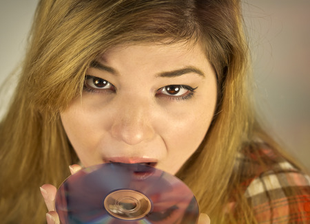 Young and cute female eating a DVD disk like a donutの写真素材