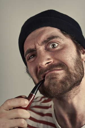 Mean bearded sailor grimacing while smoking a pipeの写真素材