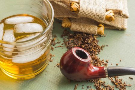 Tobacco pipe on rustic warn green wood surface with spilled natural tobacco and a glass of whisky on the rocksの写真素材