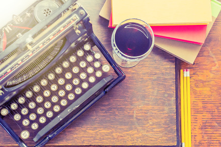 Old vintage typewriter with glass of wine pencils and books in this retro creative writing and relazation themed desk topの写真素材
