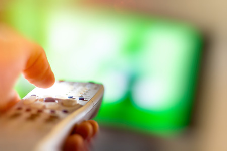 Close up of remote in hand with shallow depth of field during television watchingの写真素材