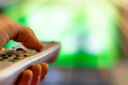 Close up of remote in hand with shallow depth of field during television watchingの写真素材