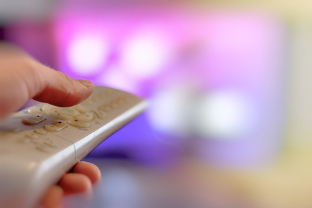 Close up of remote in hand with shallow depth of field during television watching