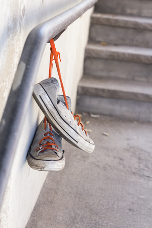 Pair of old worn classic sneakers hanging from railingの写真素材