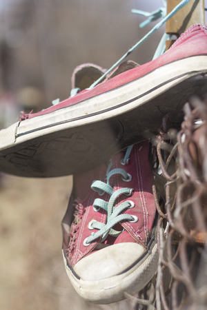 Pair of old worn classic sneakers hang from rusty chain link fenceの写真素材
