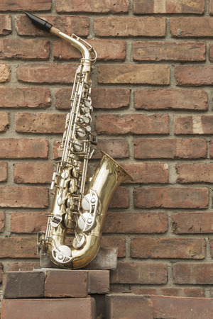 Lone old saxophone leans against brick wall outside abandoned jazz clubの写真素材
