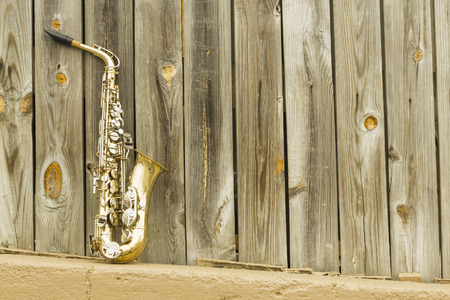 Lone old saxophone leans against wooden fence outside jazz clubの写真素材