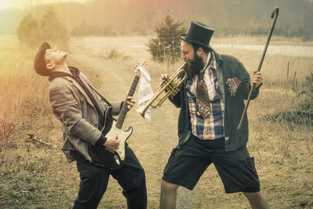 Stylish gypsies play trumpet and electric guitar on a wilderness pathの写真素材