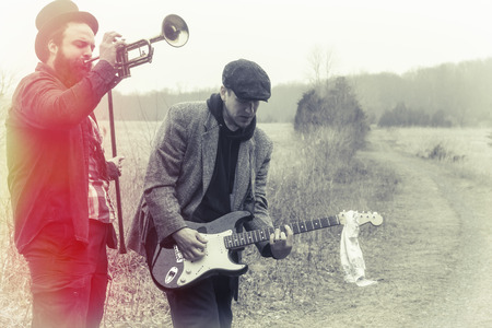 Stylish gypsies play trumpet and electric guitar on a wilderness pathの写真素材