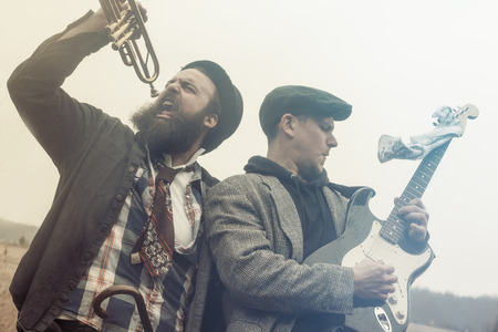 Stylish gypsies play trumpet and electric guitar on a wilderness pathの写真素材