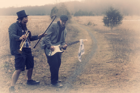 Stylish gypsies play trumpet and electric guitar on a wilderness path in grainy old fashioned grunge photoの写真素材