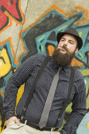 Snazzy bearded man smokes a cigarette on a city streetの写真素材