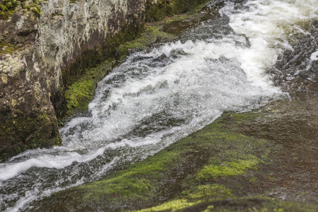 Waterfall rapids with water frozen in time splashing against mossy rocks