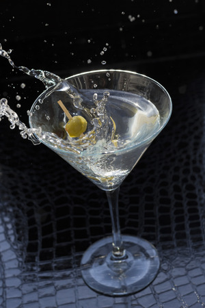 Splashing dirty martini garnished with green olives on toothpickの写真素材