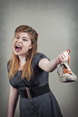 Cute girl holds up smelly stinky sneaker shoe and screamsの写真素材