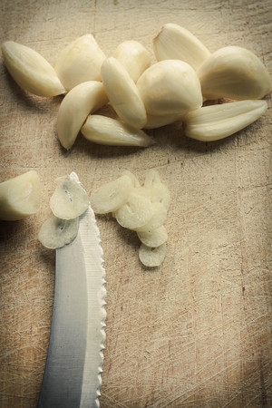 Fresh pealed garlic cloves chopped on used and worn wooden cutting board for food ingredient backgroundの写真素材