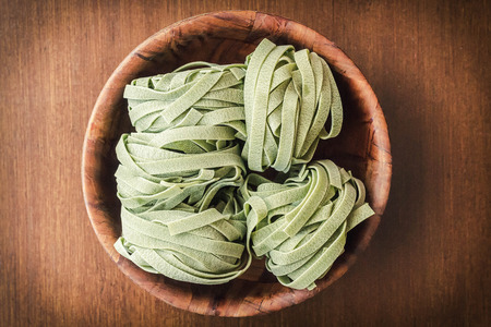 Dry organic spinach fettuccine pasta nests in a wooden bowlの写真素材