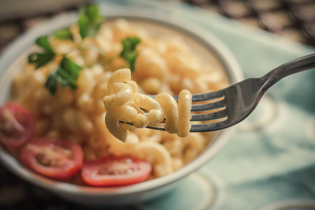 Delicious macaroni and cheddar cheese with fresh sliced grape tomatoes and parsley sprigの写真素材