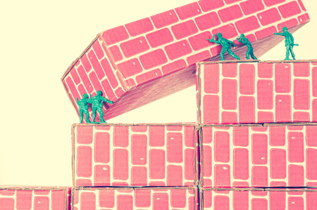 Green army men using teamwork to make progress up the toy brick stairsの写真素材