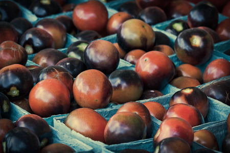 Red and purple organic plum tomatoes on display at farmers marketの写真素材