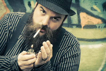 Snazzy bearded man lights a cigarette on a city streetの写真素材