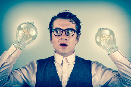Nerdy four eyed businessman is shocked by his lightbulb handsの写真素材