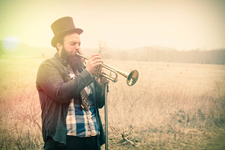 Stylish bearded gypsy plays trumpet on a wilderness pathの写真素材