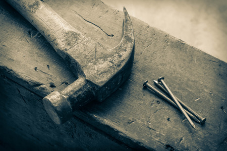 Old and worn contracting hammer and three nails on a distressed work benchの写真素材