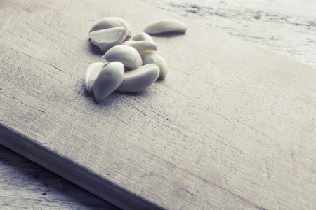 Fresh pealed garlic cloves on used and worn wooden cutting board for food ingredient background