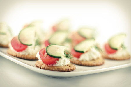 Snack plate of crackers topped with tomato cucumber dill and cheeseの写真素材
