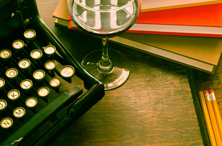 Old vintage typewriter with glass of wine pencils and books in this retro creative writing and relazation themed desk topの写真素材