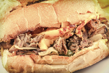 A messy Philly Cheesesteak with onions peppers and mushrooms, onion rings on the sideの写真素材