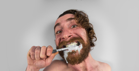 Silly bearded man brushing teeth in bathroom mirrorの写真素材