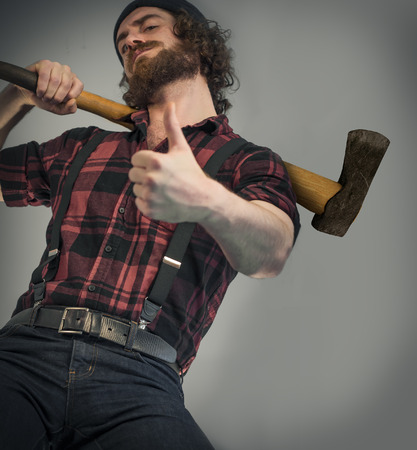 Silly hipster lumberjack gives thumbs up sign while holding axeの写真素材