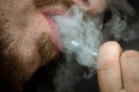 Bearded man smokes a vape e-cigarette in extreme closeup macro