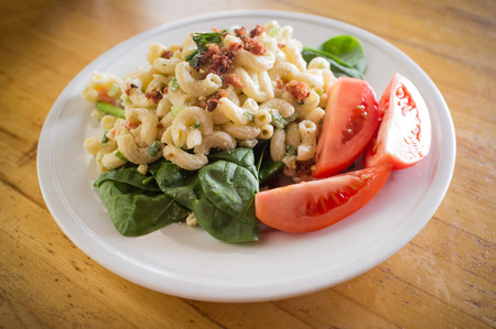 Macaroni salad on bed of spinach greens with tomato wedges and bacon bitsの写真素材