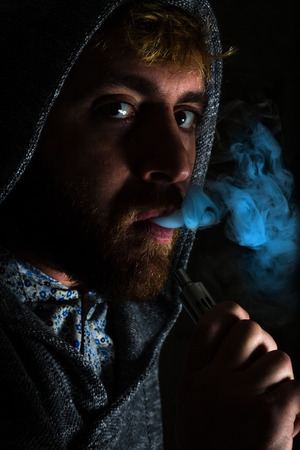 Dramatic lighting bearded man smokes a vape e-cigaretteの写真素材