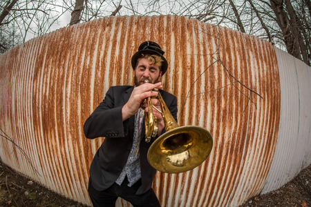 Stylish bearded gypsy plays trumpet by rusty fenceの写真素材